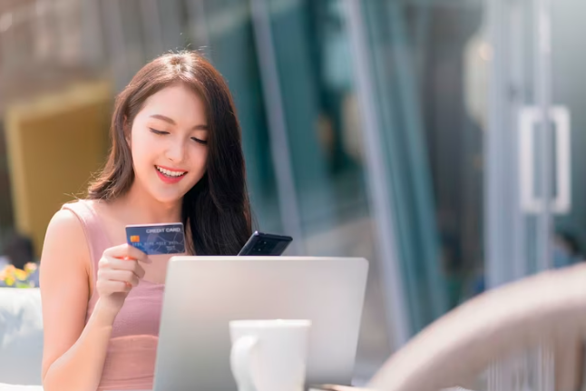 A smiling asian woman holding a credit card.