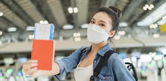 Woman holding plane ticket wearing mask