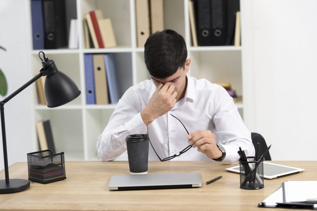 tired man sitting in front of his desk with laptop and coffee