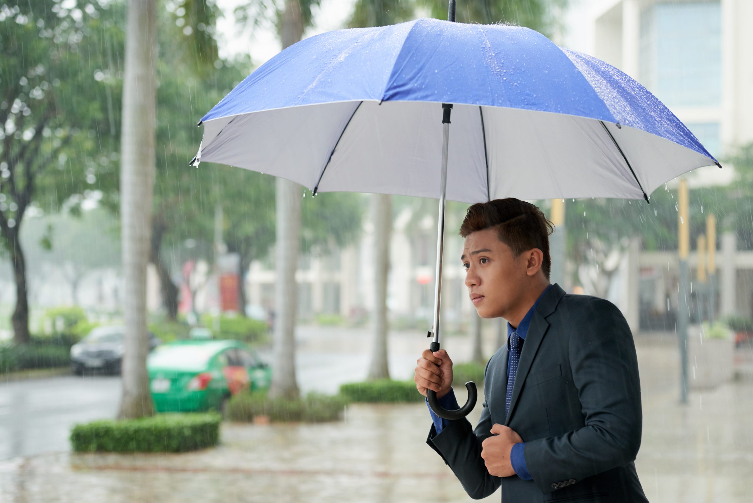 Man in a business suit holding an umbrella in rainy weather.