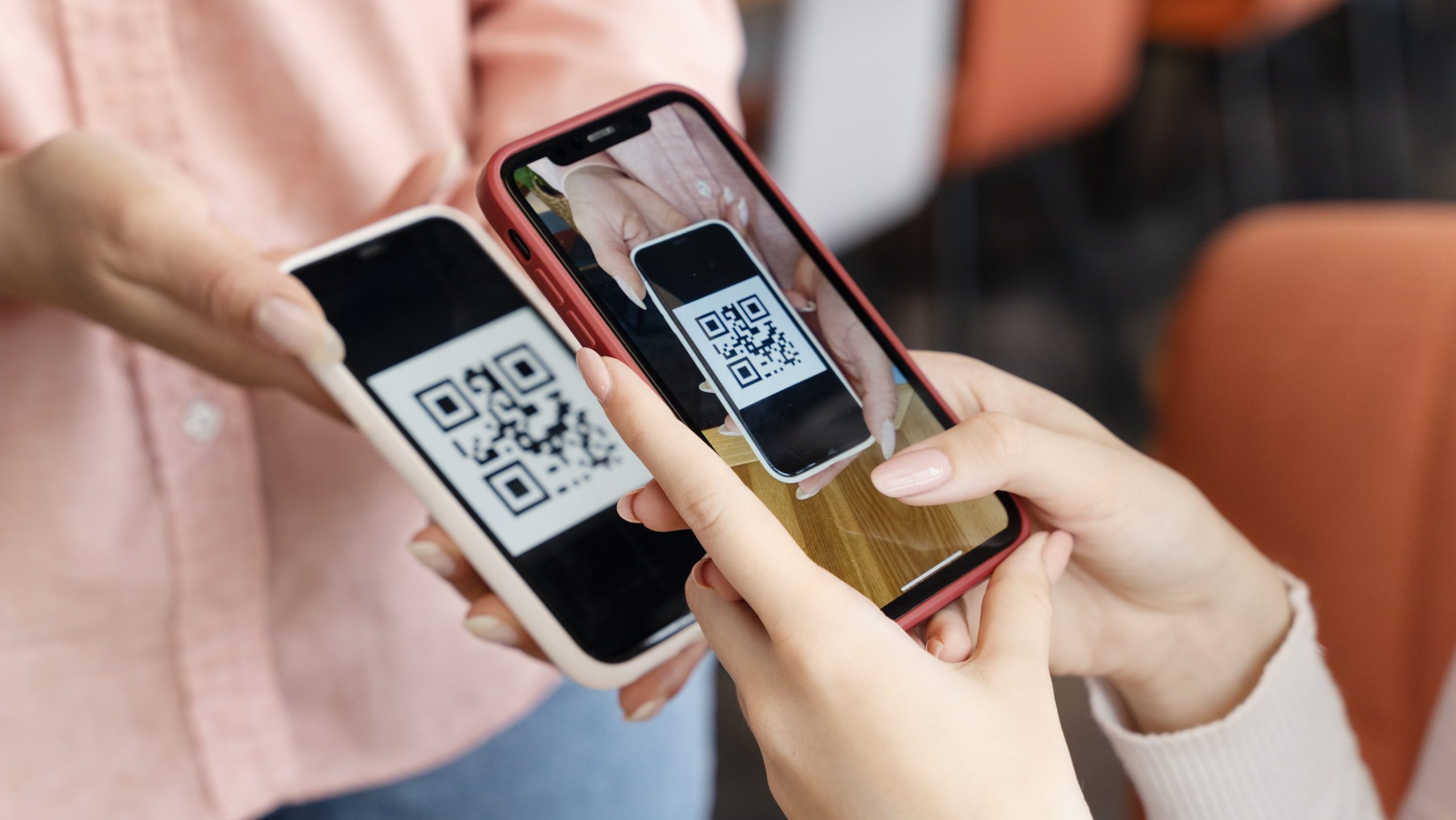 Person's hand holding a smartphone, scanning QR code from another phone.