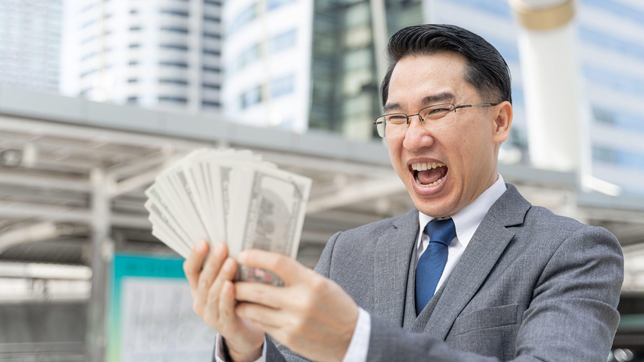 Happy Asian man with glasses holding a fan of money.