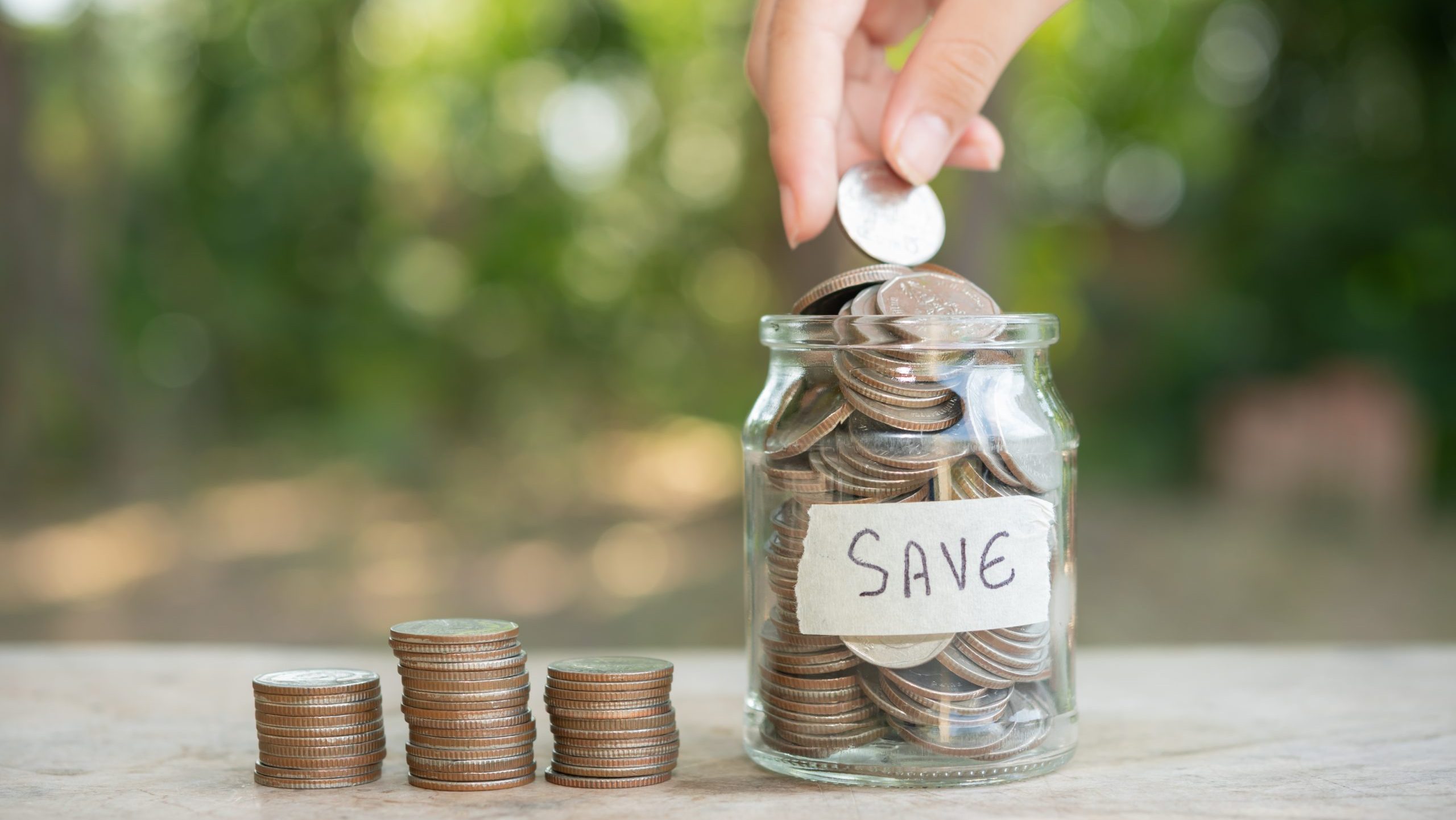 Hand putting coin on a glass jar labeled save.