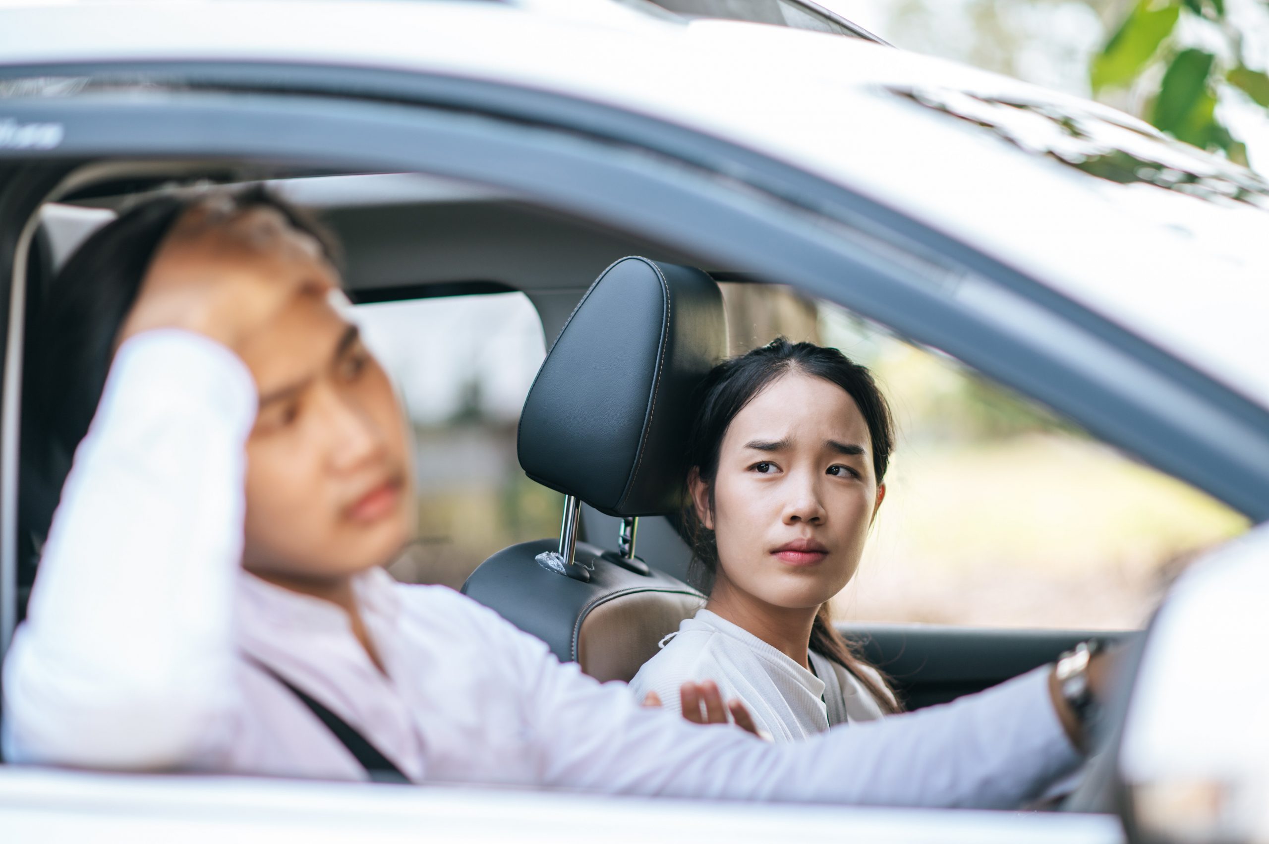 A woman on the passenger seat looking at frustrated male driver.