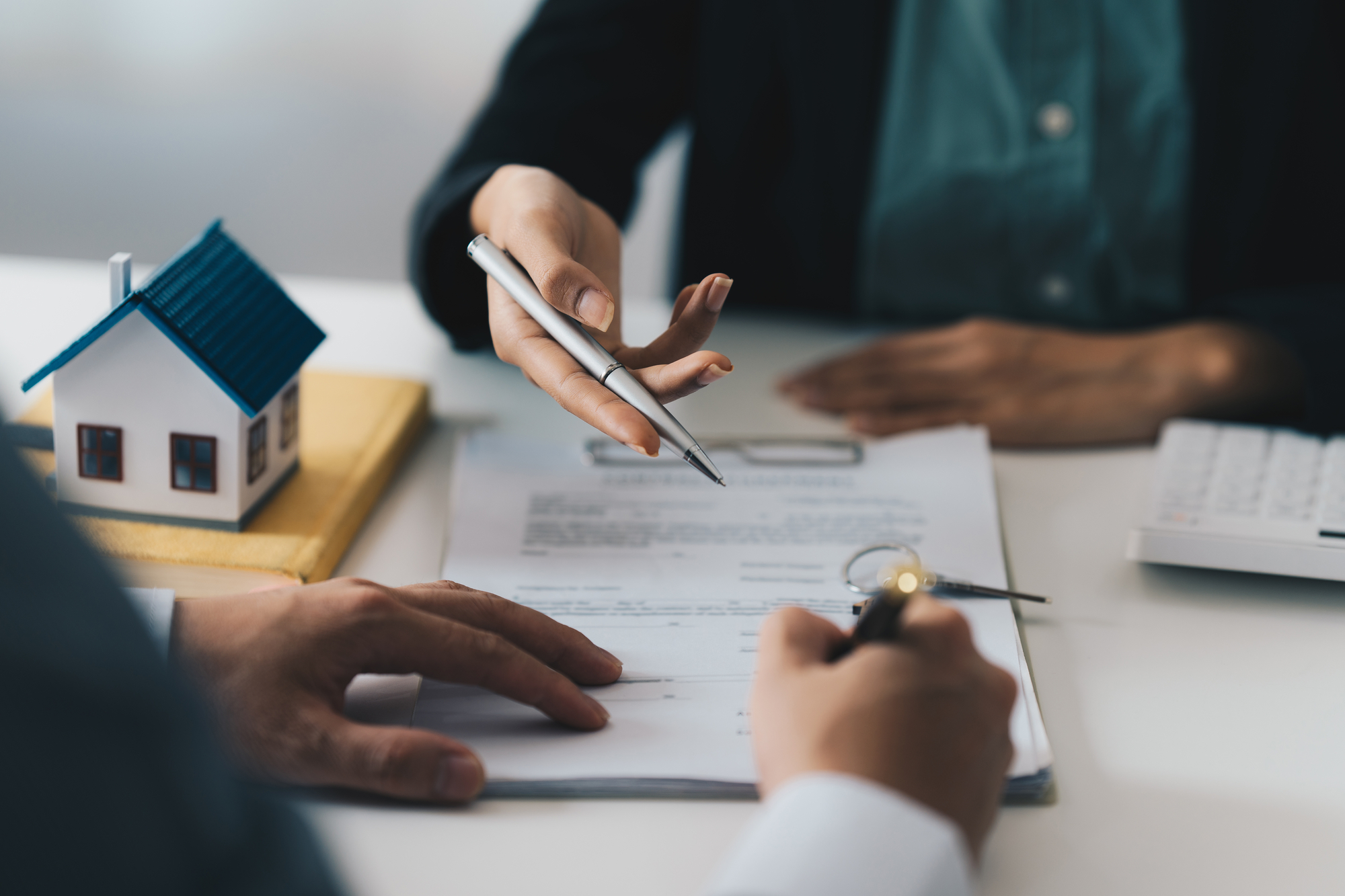 Hands of two people signing a contract with a small house on the table.