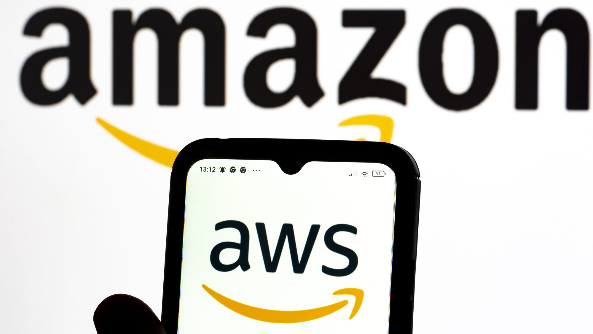 Hand holding phone with AWS logo and an amazon logo in the background.