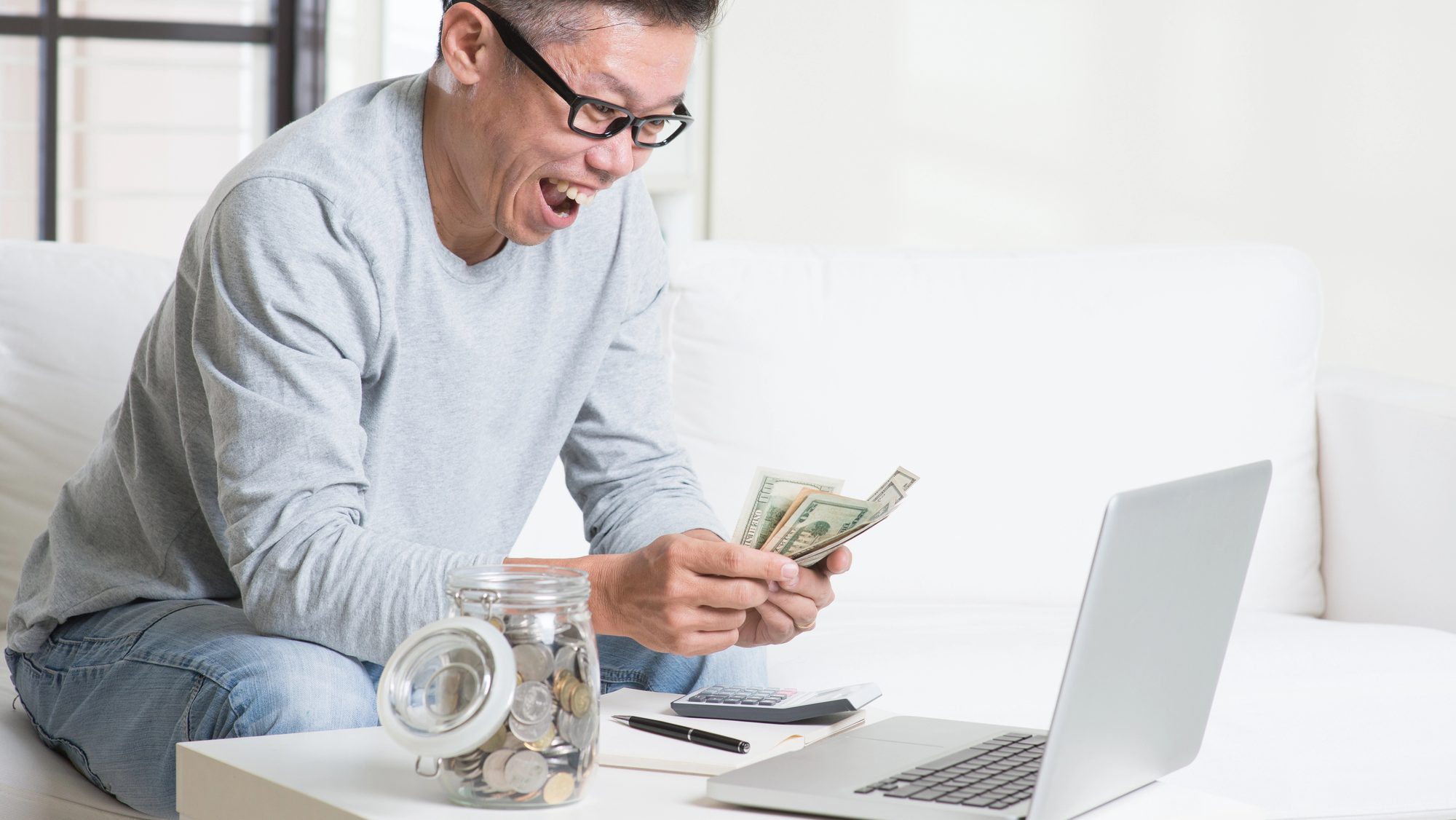 Man counting money in front of his computer and coin jar.