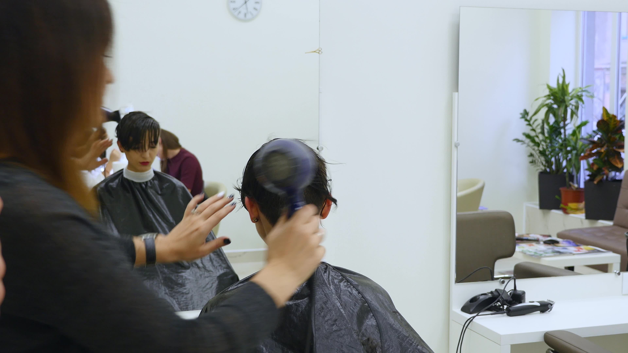 Hairdresser drying and brushing hair of female in hair salon.