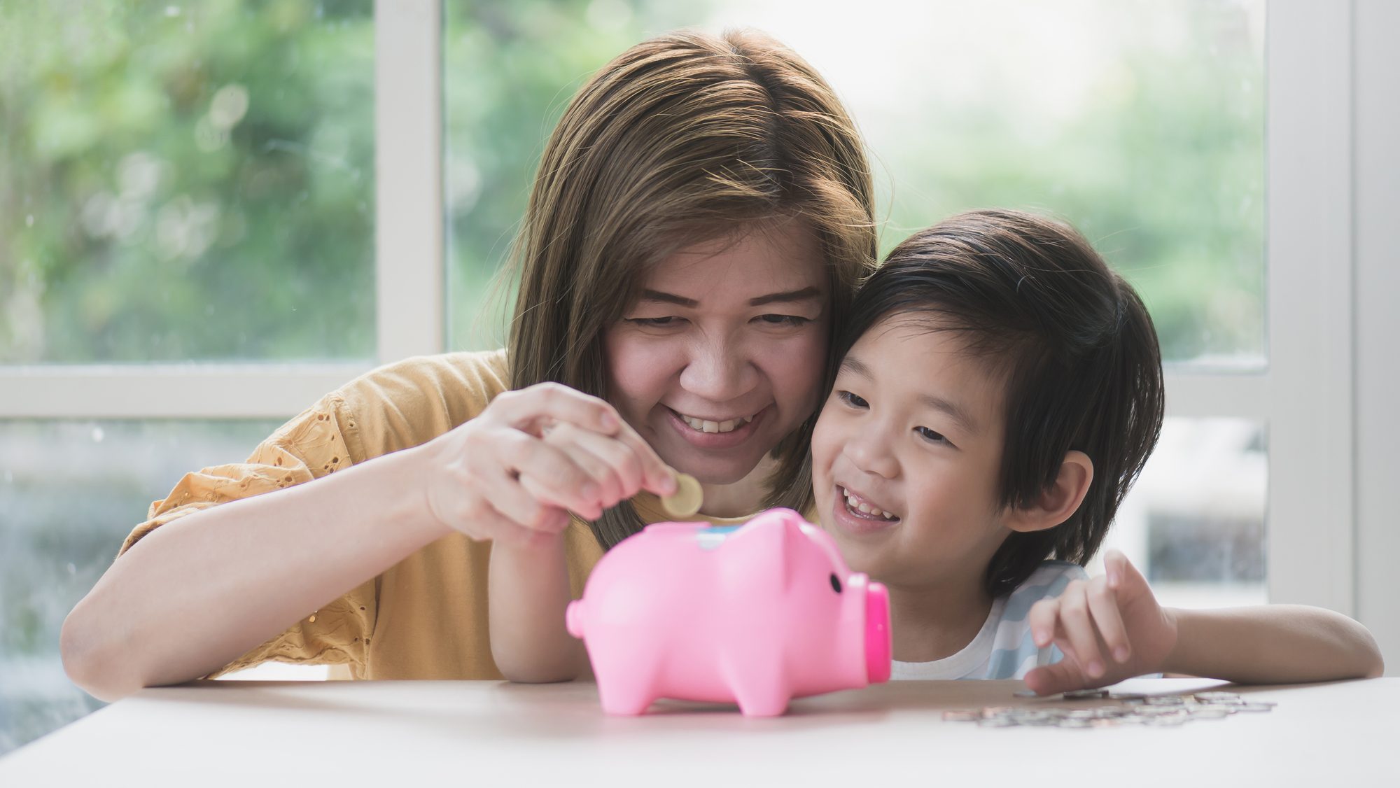 Asian mother and her child putting a coin into a piggy bank.