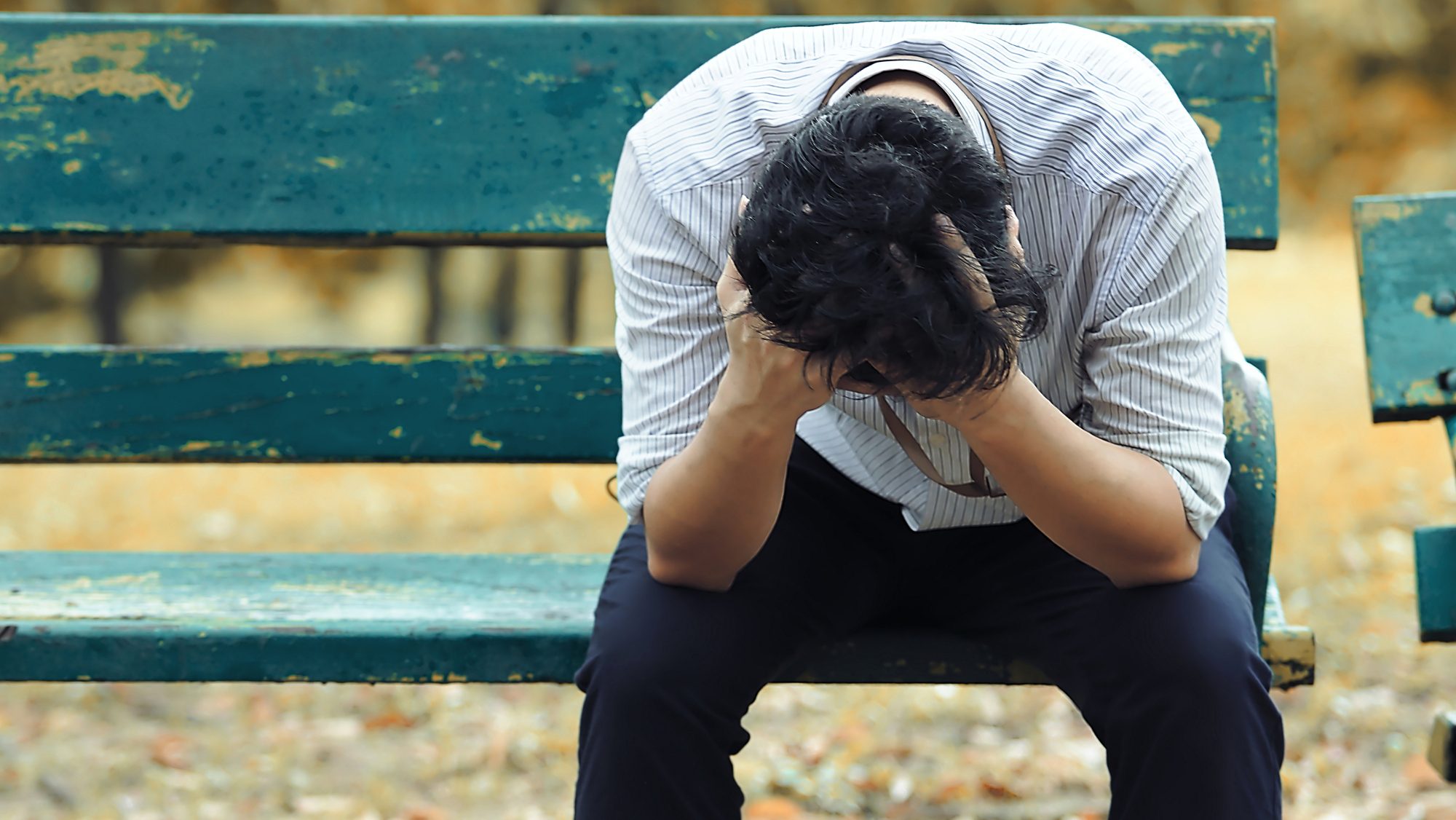 Frustrated stressed Asian business man with hand cover face sitting on the bench of public park.