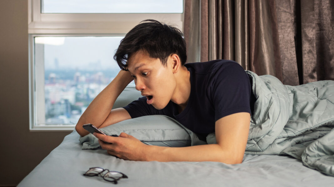Man looking at phone and shocked on bed.