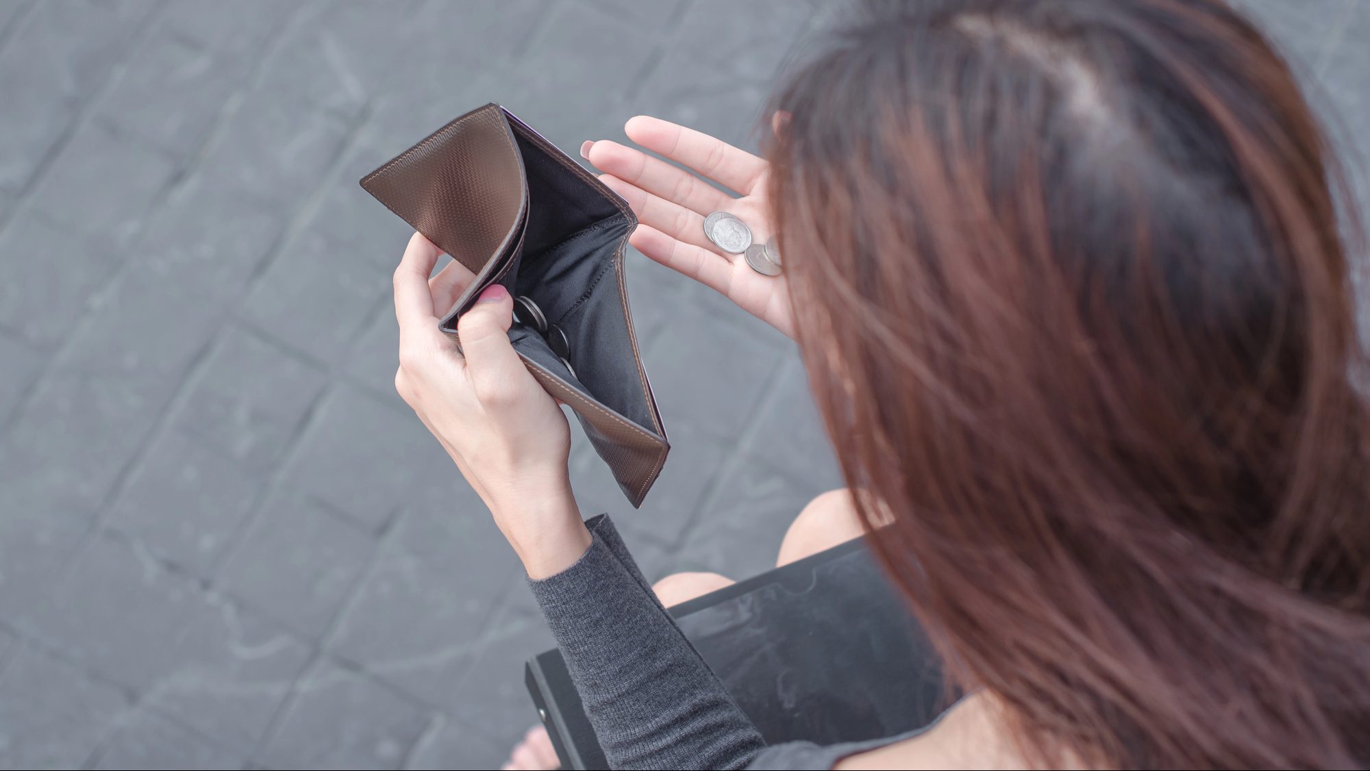 Woman looking at an empty wallet with a few coins in one hand.