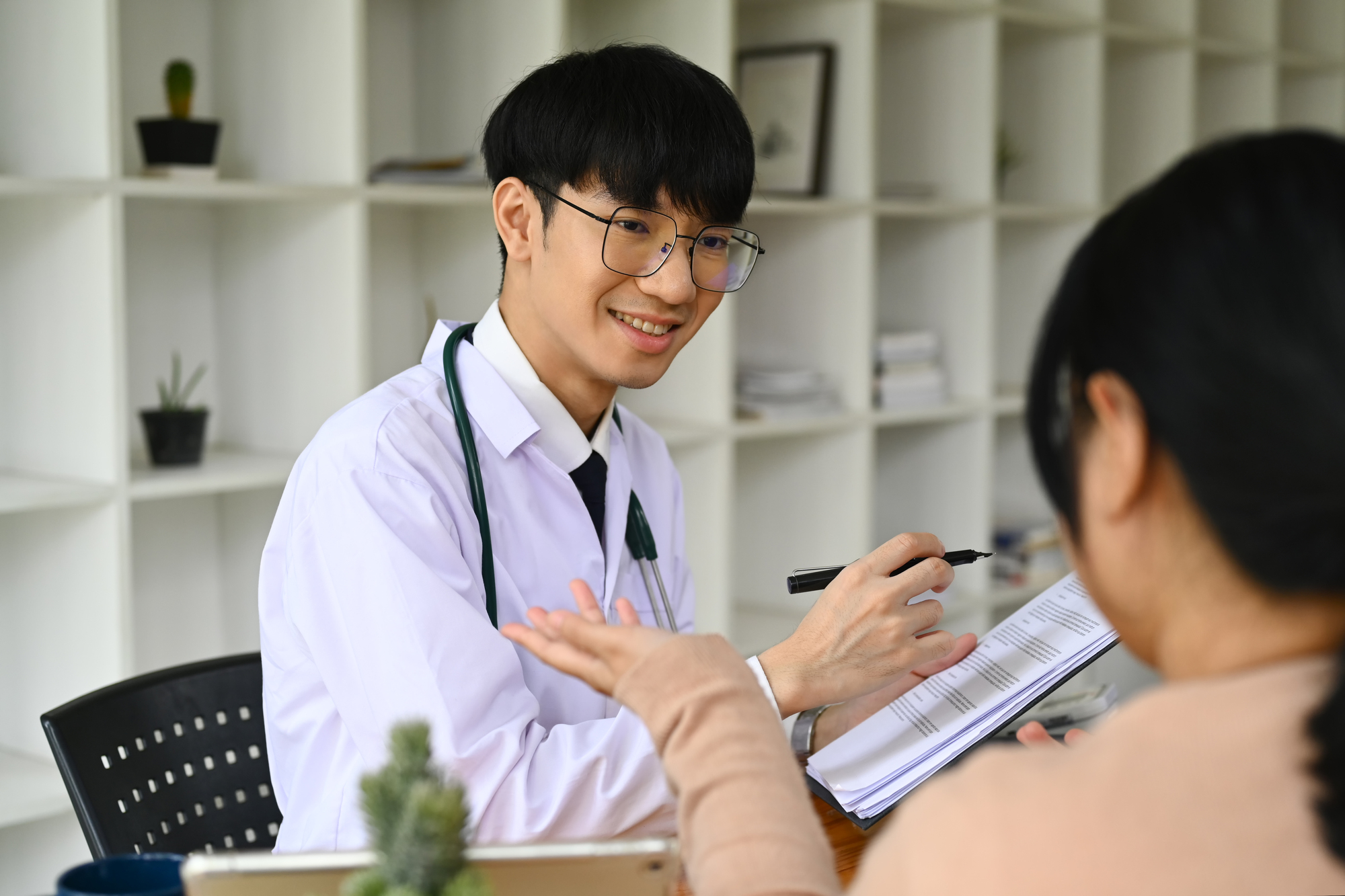 Positive male doctor in white medical uniform giving consultation, explaining treatment to female patient.