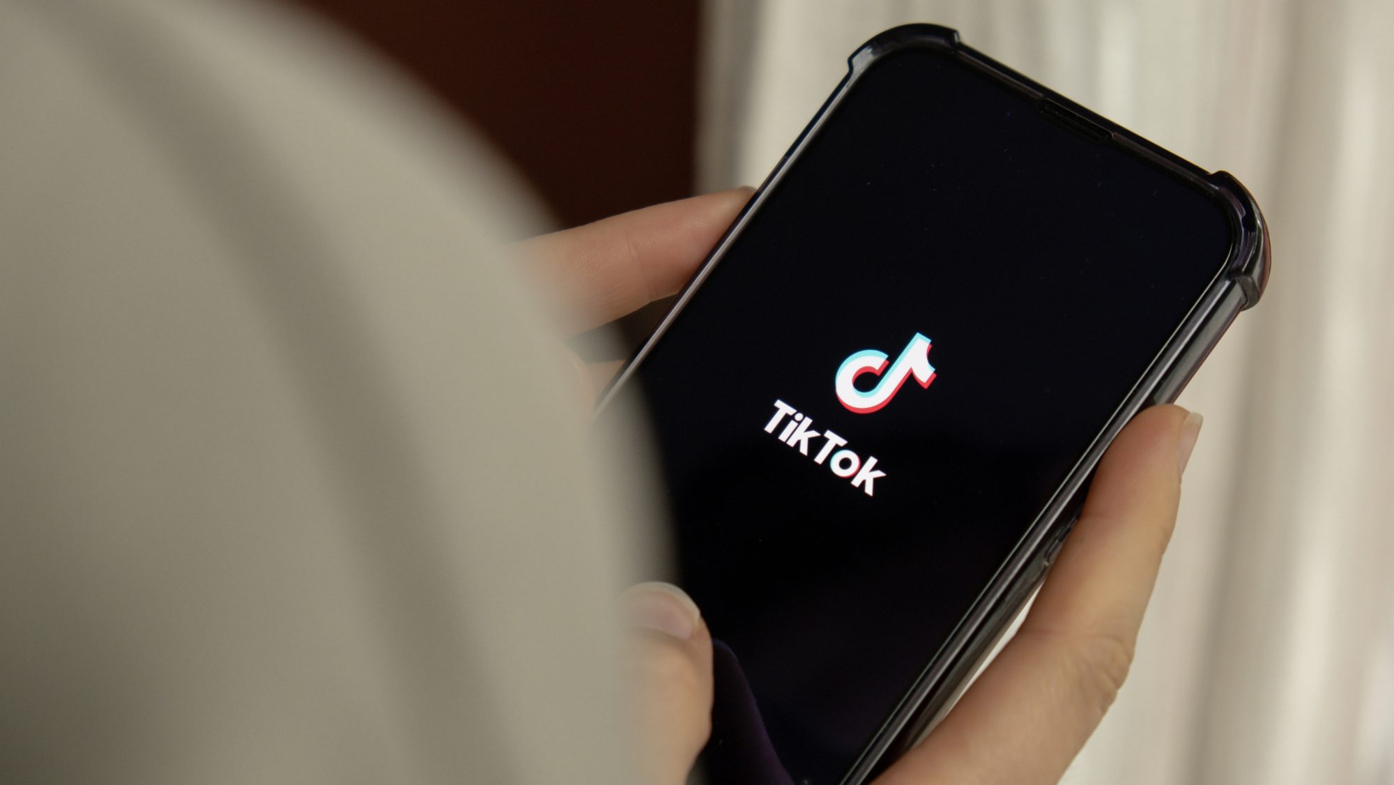 Female hand holding phone with TikTok icon on screen.