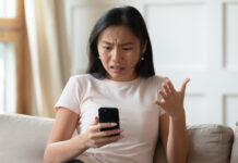 Scammers kick off Fire Horse year, with Millennials and Gen Z most at risk Mad Asian woman sitting on a couch while holding her smartphone.