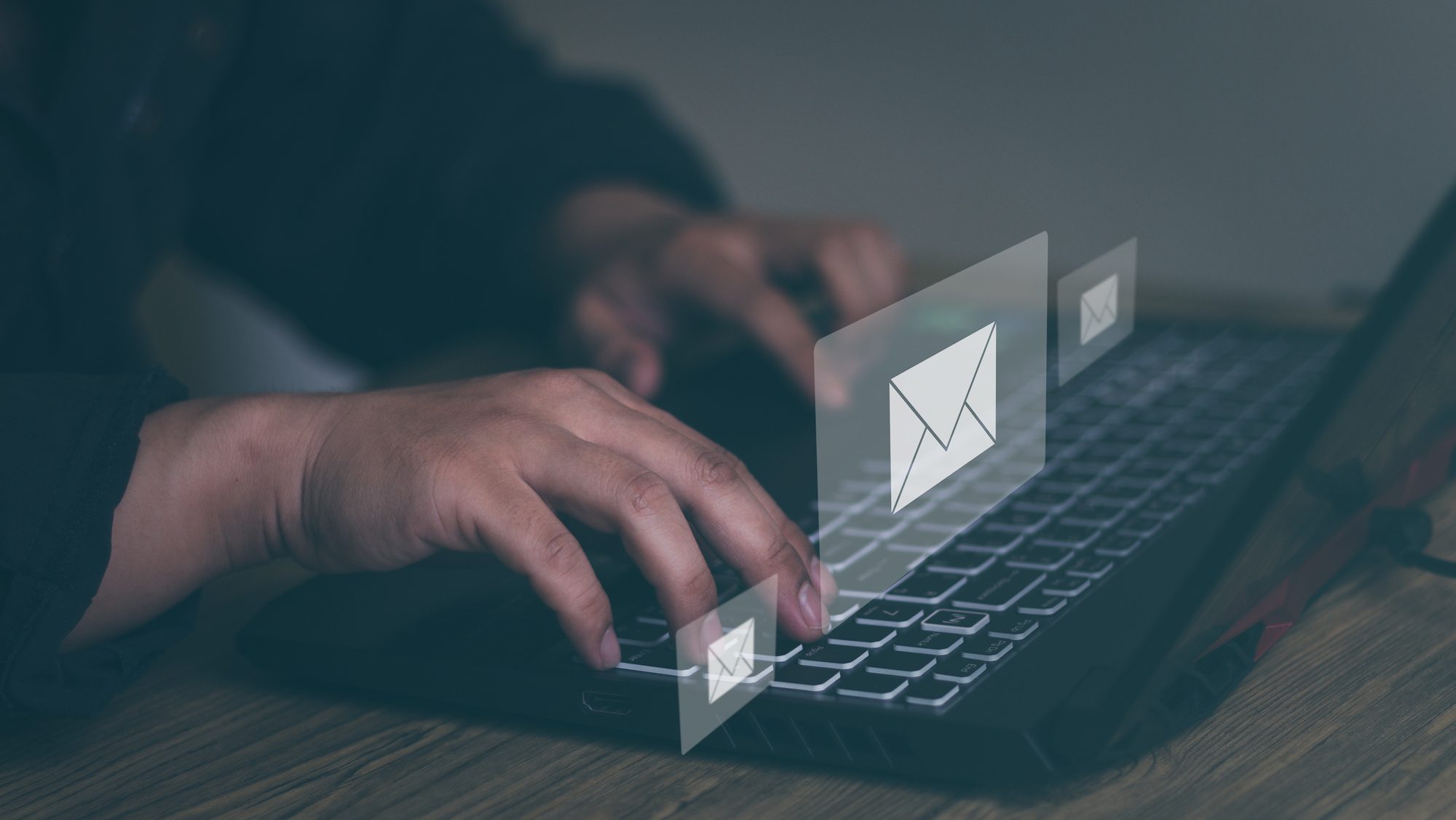 Man's hand typing on a laptop with email popping.