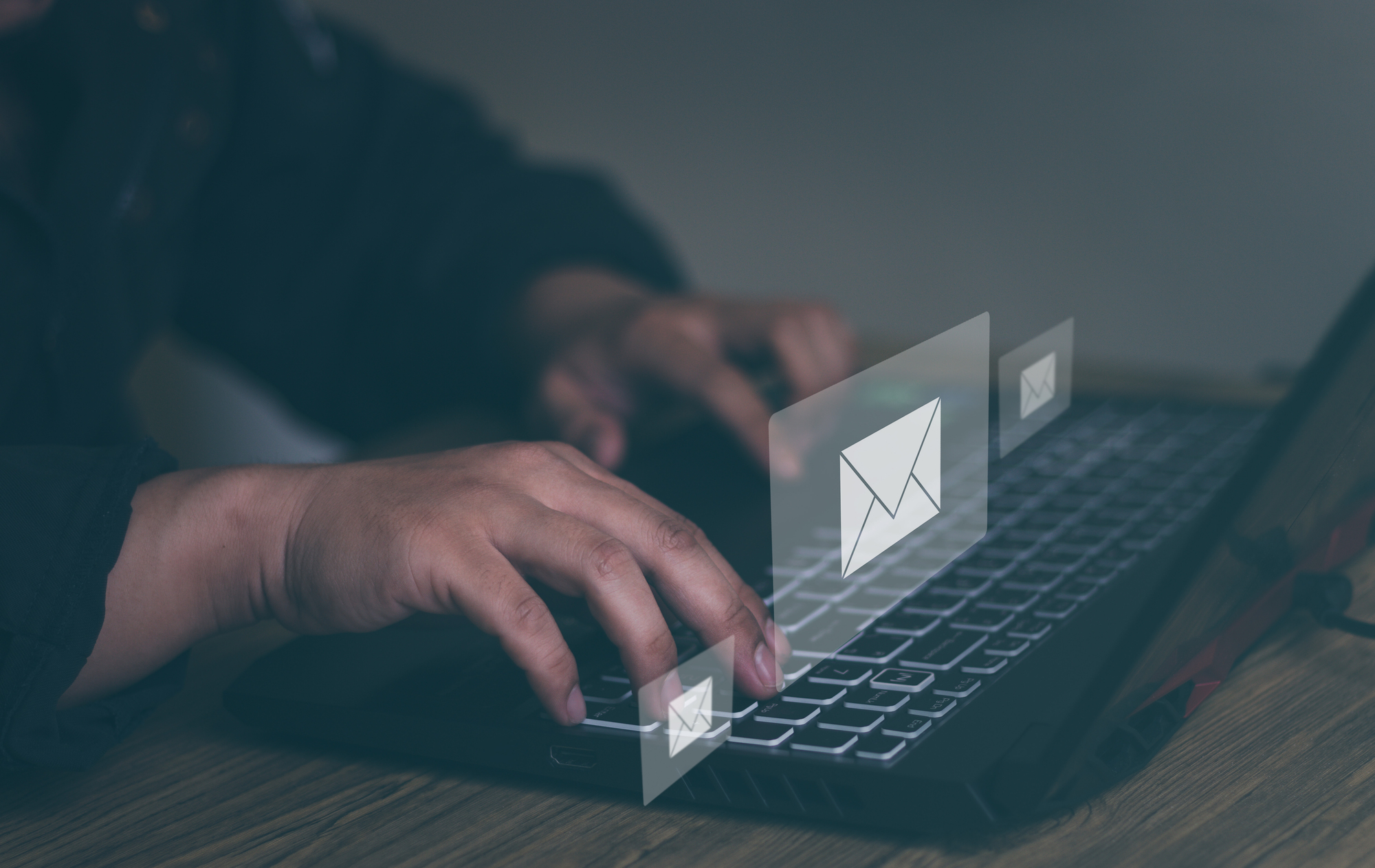 Man's hand typing on a laptop with email popping.