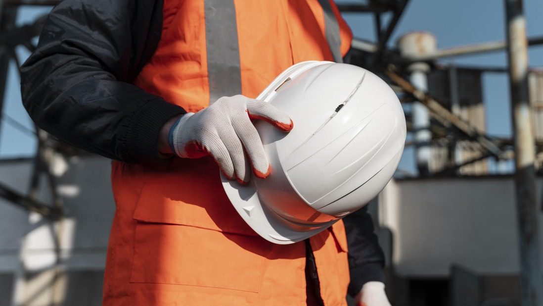 Construction worker holding white helmet, wearing PPE