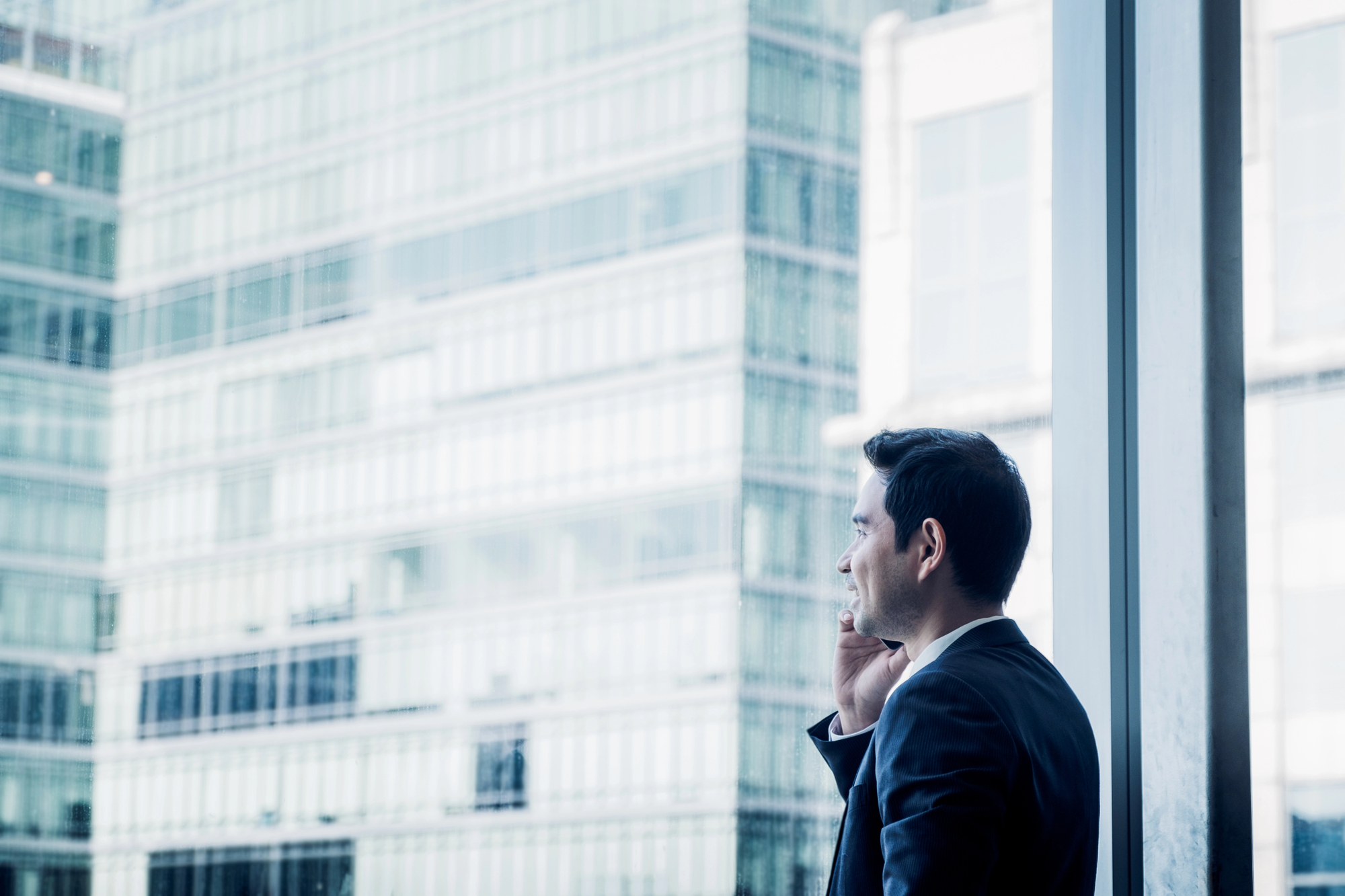 Businessman using mobile phone near office window at office.