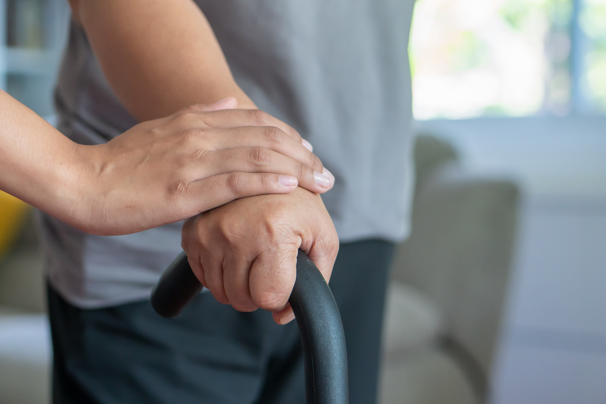 old senior woman with walking disability using cane as walking aid, with helping hand of care giver or nurse