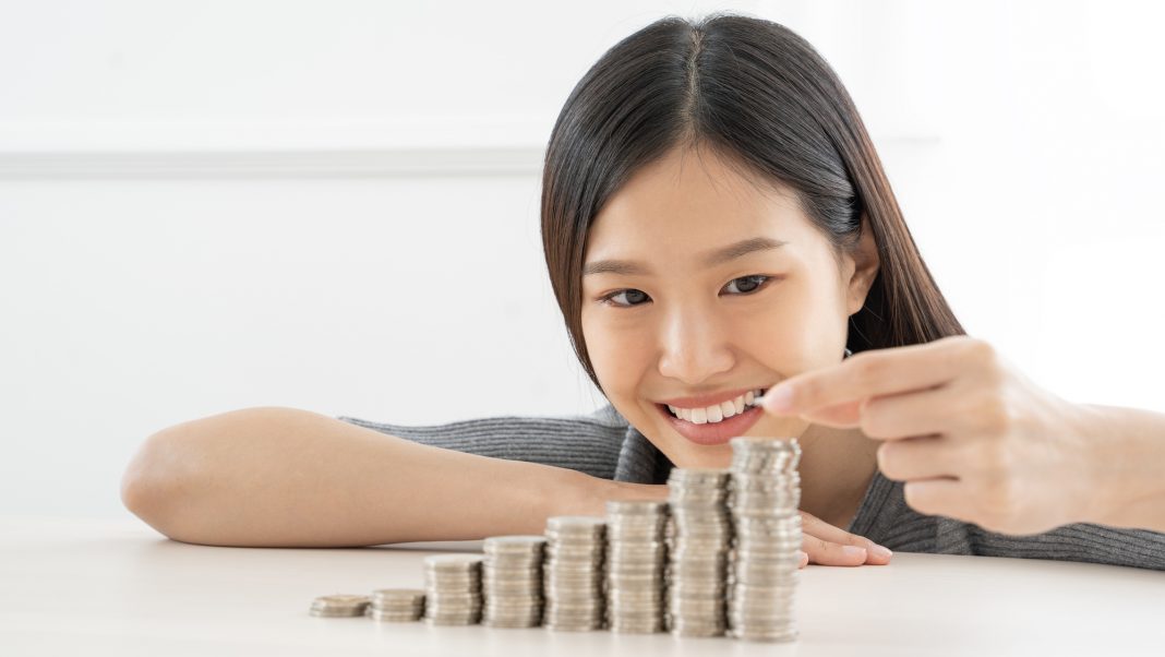 Young Asian woman making stack of coins.