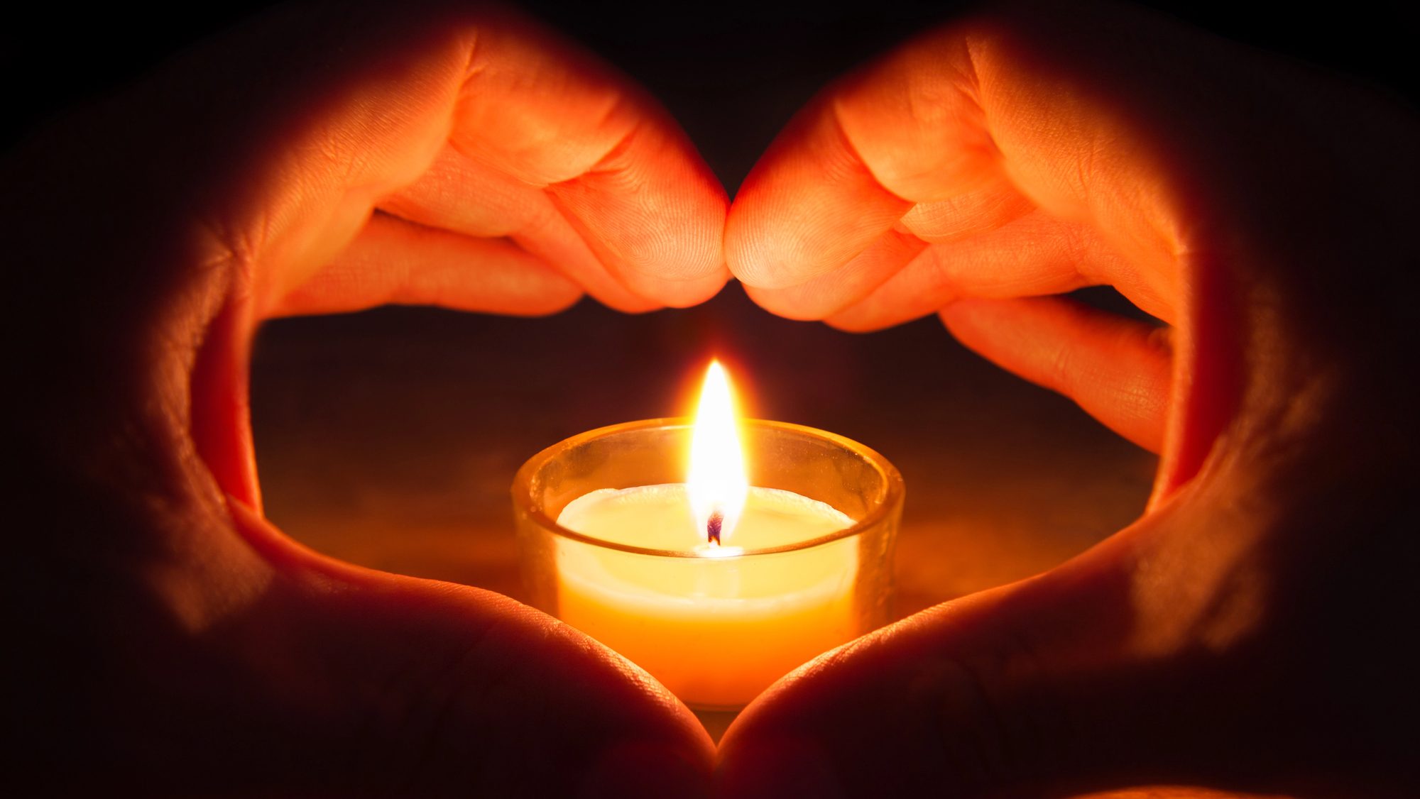 A lit candle and hands forming a heart shape.