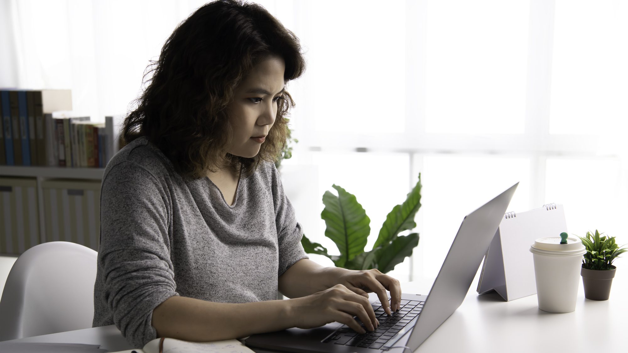 Young Asian businesswoman working on laptop at home. Female student sitting on desk study online on laptop take notes in notebook