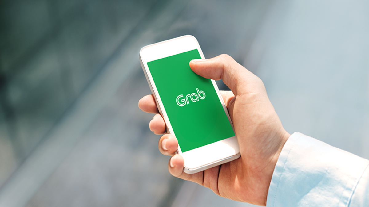 Man's hand holding white phone with Grab logo.