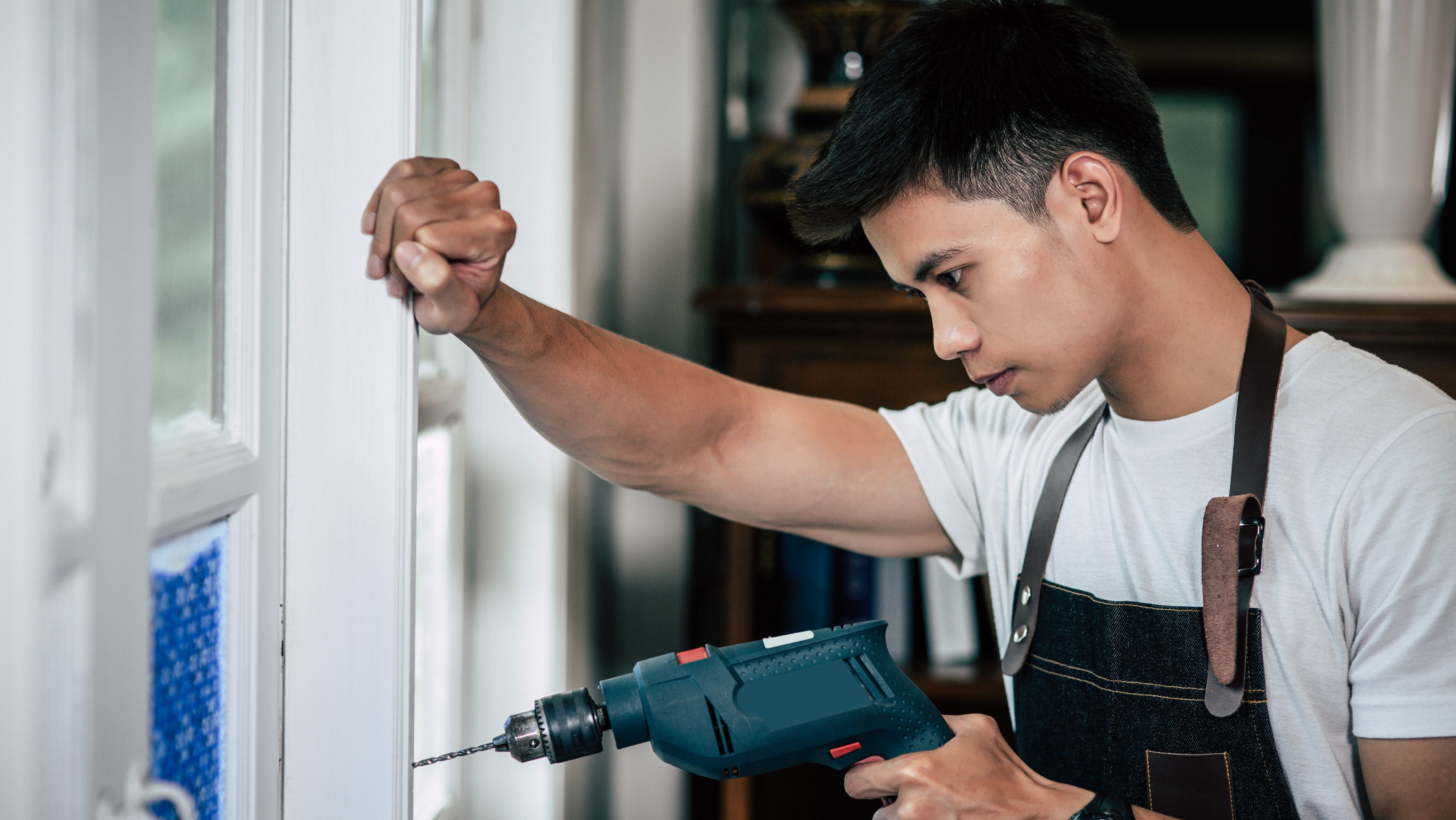 The carpenter holds the drill and drills the window.