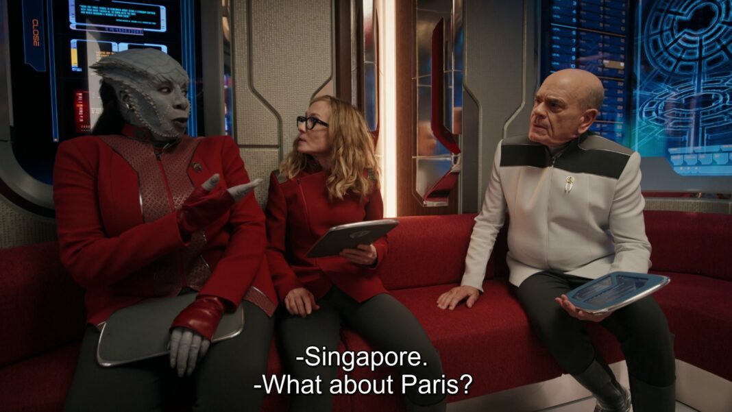 Three characters in a futuristic setting sit on a red couch: a reptilian alien, a woman wearing glasses, and an older man in a white uniform, each holding a device. Text reads, 