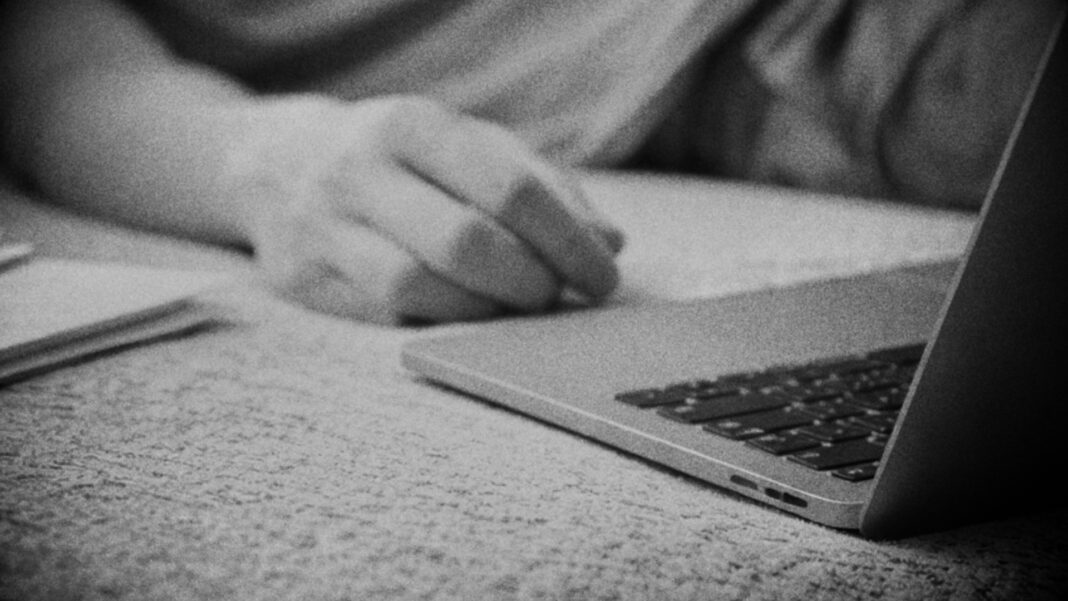 A man lies exhausted on a sofa beside an open laptop and unfinished paperwork; the quiet toll of prolonged overwork is captured.