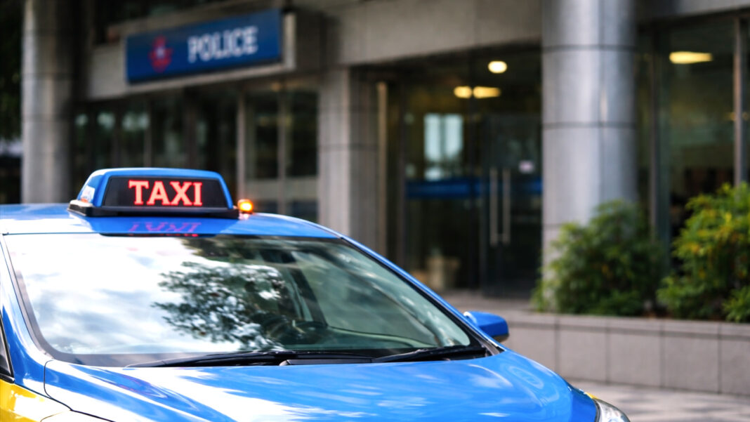 Close-up of a blue-yellow taxi parked outside a modern civic building